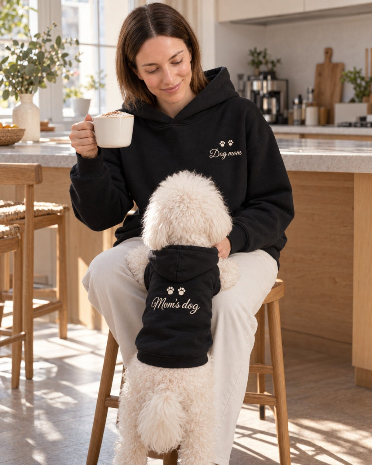 Donna in cucina con Ben, felpe nere abbinate Dog mom e Mom's dog con ricamo panna sulla schiena del cane