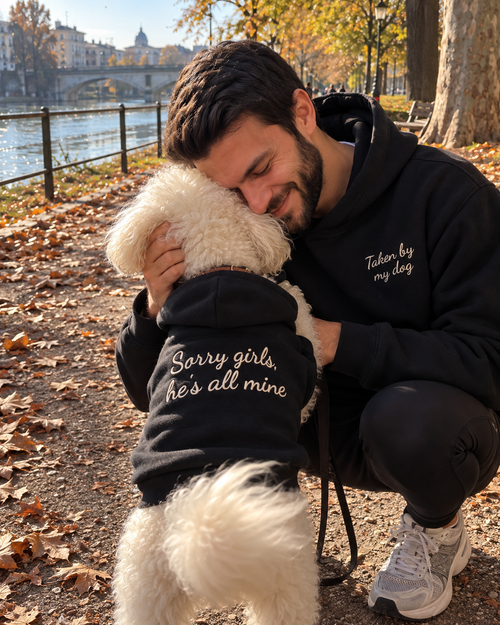 Set felpe abbinate Taken by my dog + Sorry girls, he's all mine nero: uomo abbraccia il cane in felpa ricamata lungo il fiume in autunno